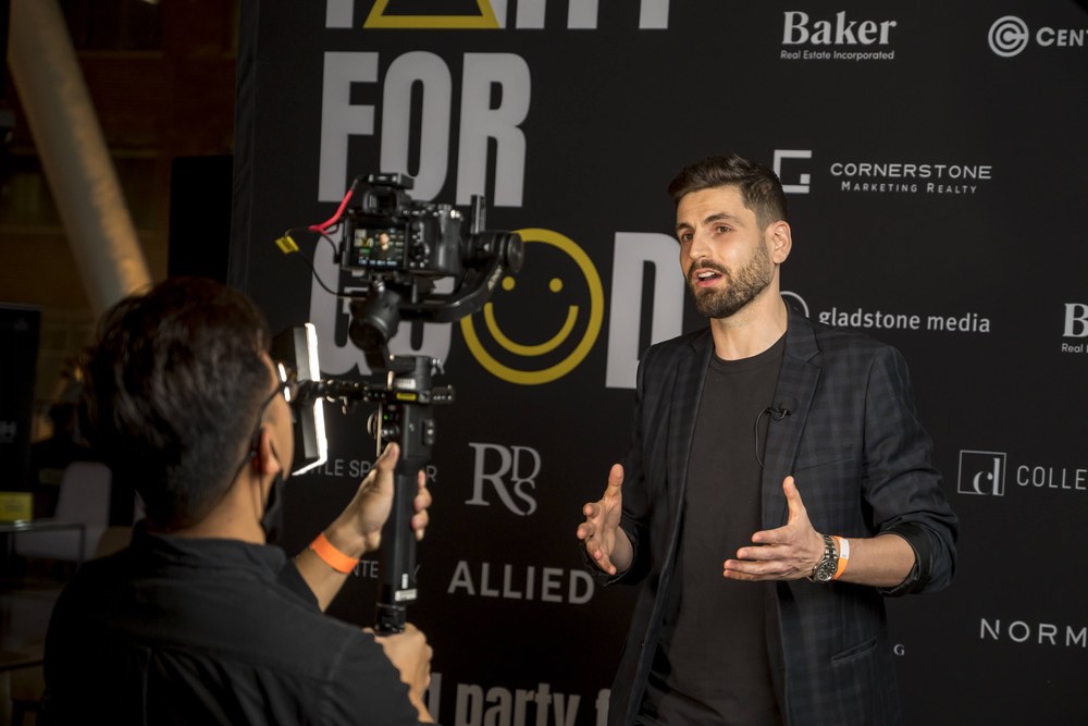 Charles Jaque speaking to camera at the Party for Good gala, in front of the event's sponsor wall